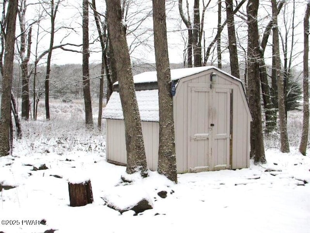 snow covered structure featuring an outbuilding and a storage shed