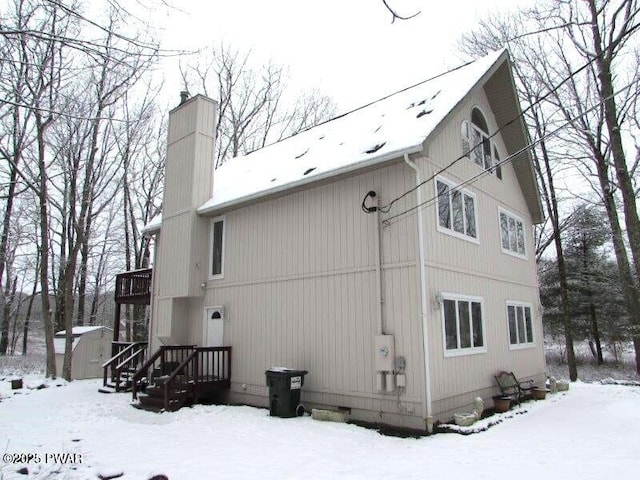 view of snowy exterior with a shed, a chimney, and an outdoor structure