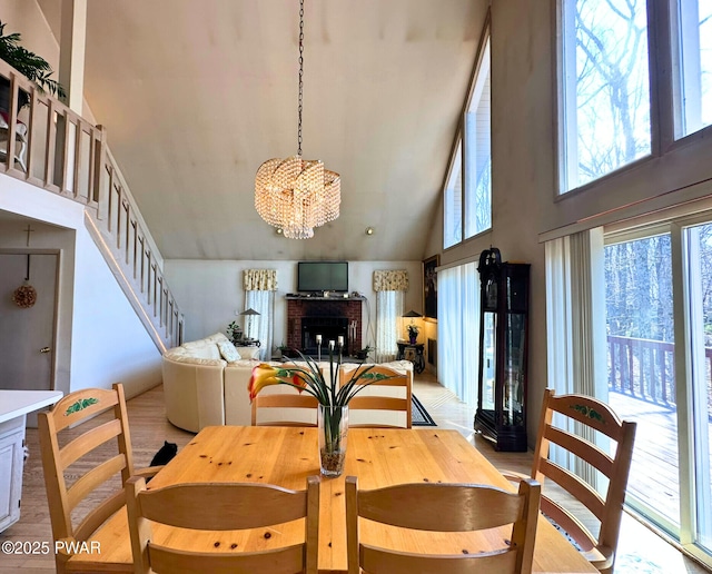 dining area with stairway, a fireplace, light wood finished floors, high vaulted ceiling, and a notable chandelier