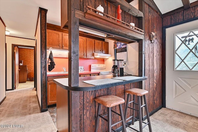 kitchen featuring light carpet, white range with electric cooktop, wooden walls, and a breakfast bar area