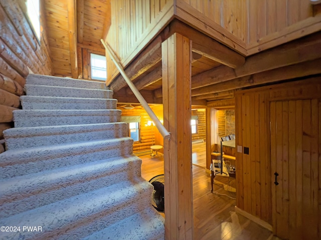 stairs with hardwood / wood-style floors, beam ceiling, wood ceiling, and log walls