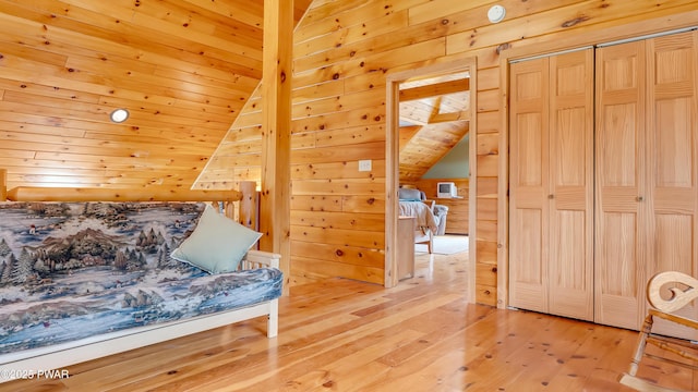 bedroom with a closet, lofted ceiling, wooden walls, wood ceiling, and light wood-style flooring