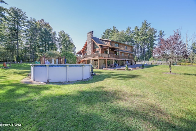 rear view of property featuring a chimney, a lawn, an outdoor pool, and a deck