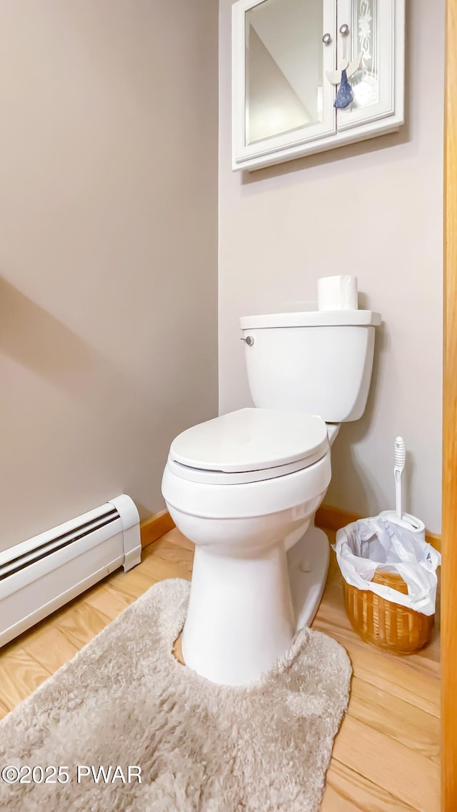 bathroom featuring baseboard heating, toilet, baseboards, and wood finished floors