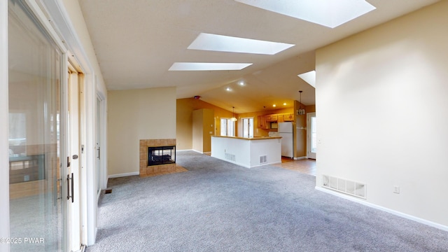 unfurnished living room with a tiled fireplace, light colored carpet, and vaulted ceiling