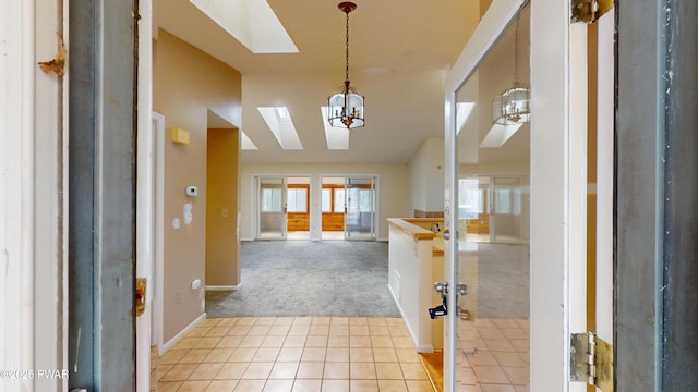 foyer with lofted ceiling with skylight, an inviting chandelier, and light carpet