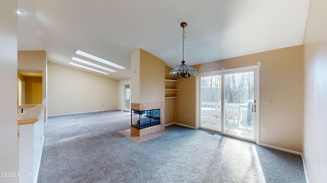 unfurnished living room with a tile fireplace, carpet floors, vaulted ceiling with skylight, and a chandelier