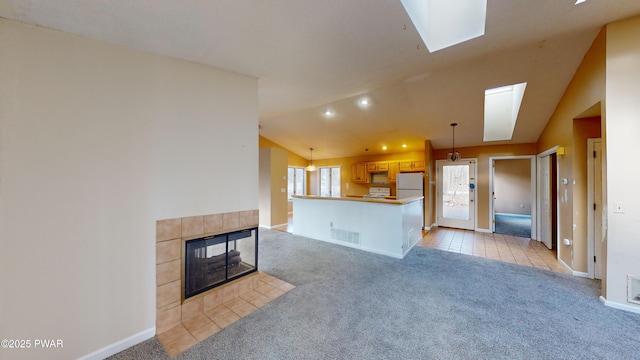 living room with a tile fireplace, light colored carpet, and lofted ceiling with skylight