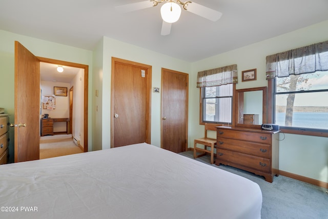 bedroom with ceiling fan, a water view, light colored carpet, and two closets