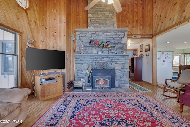 living room with wood-type flooring, a stone fireplace, ceiling fan, and a high ceiling