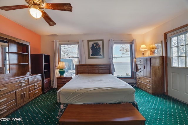 bedroom with multiple windows, ceiling fan, carpet floors, and a baseboard heating unit