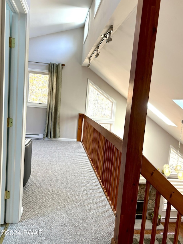 corridor featuring carpet flooring, lofted ceiling with skylight, a baseboard radiator, and track lighting