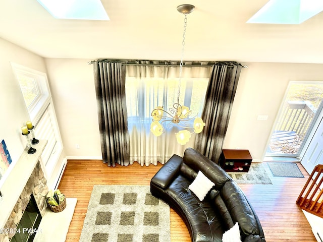 sitting room with hardwood / wood-style floors, a stone fireplace, baseboard heating, and a skylight