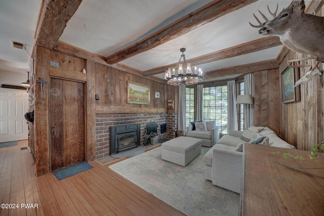 living room featuring a wood stove, an inviting chandelier, beamed ceiling, wood walls, and light hardwood / wood-style floors