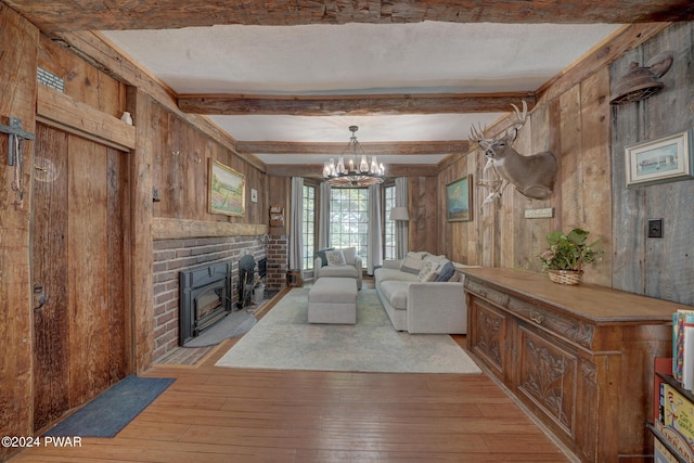 living room featuring a textured ceiling, light hardwood / wood-style flooring, a notable chandelier, beamed ceiling, and wood walls