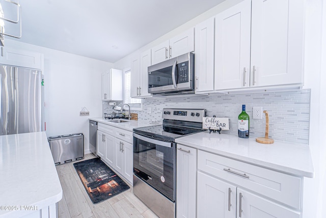 kitchen featuring sink, light hardwood / wood-style flooring, stainless steel appliances, tasteful backsplash, and white cabinets