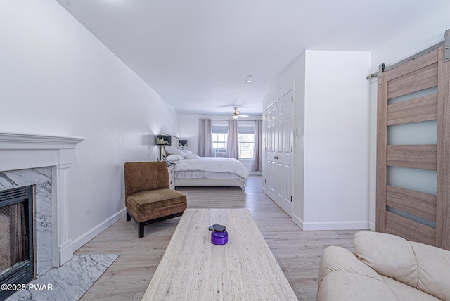 bedroom featuring a barn door, a high end fireplace, and light hardwood / wood-style flooring