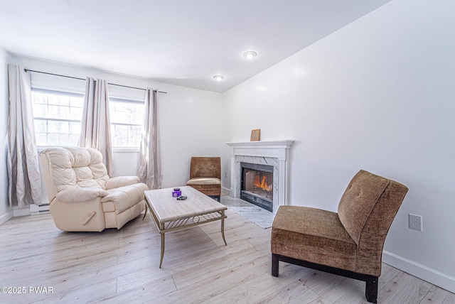 living area with a baseboard radiator, a premium fireplace, and light hardwood / wood-style floors