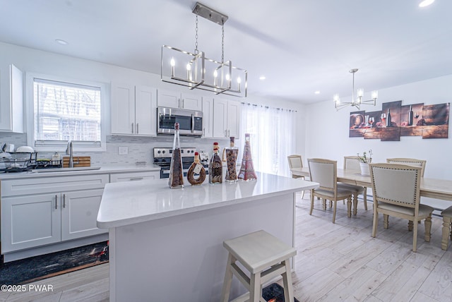 kitchen with sink, white cabinetry, a center island, hanging light fixtures, and appliances with stainless steel finishes