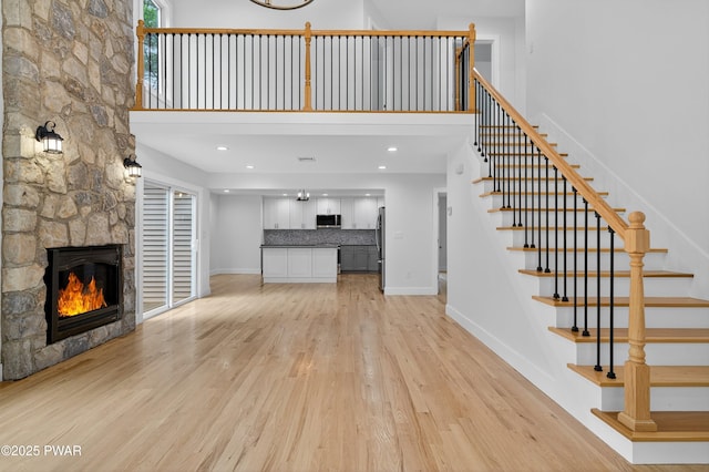 120 Milford Estates Dr, Milford, PA 18337 - unfurnished living room with light wood-type flooring, stairs, a stone fireplace, a high ceiling, and recessed lighting