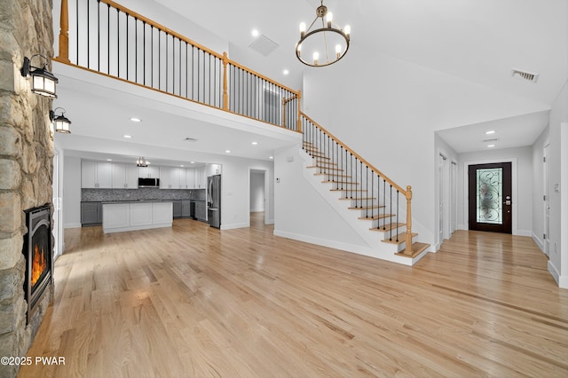 120 Milford Estates Dr, Milford, PA 18337 - unfurnished living room featuring light wood-style flooring, stairs, a stone fireplace, a chandelier, and a towering ceiling