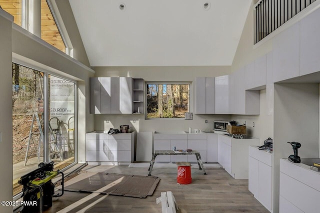 kitchen featuring white cabinetry, light hardwood / wood-style flooring, and high vaulted ceiling