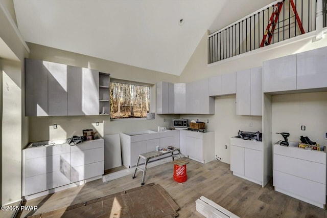 kitchen with white cabinetry, high vaulted ceiling, and light wood-type flooring