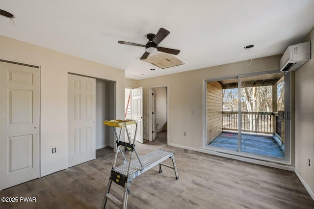 interior space with a wall mounted air conditioner, wood-type flooring, and ceiling fan