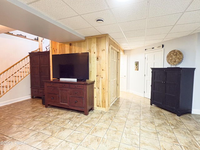 living room with wood walls, stairs, a drop ceiling, and baseboards