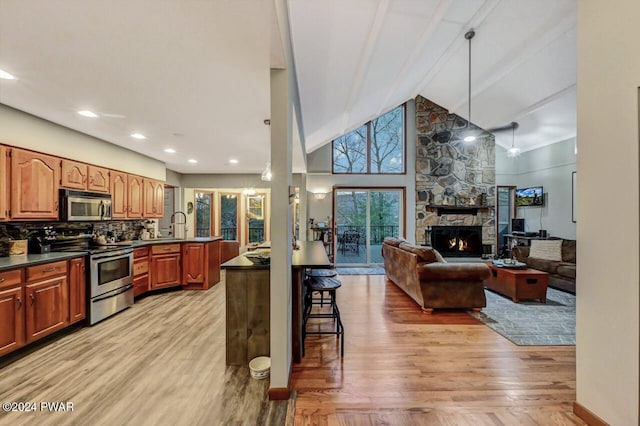 kitchen featuring appliances with stainless steel finishes, hanging light fixtures, a kitchen breakfast bar, a fireplace, and light hardwood / wood-style floors