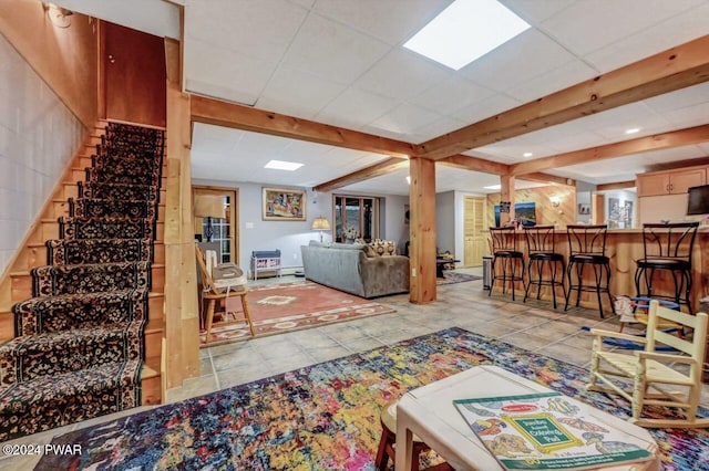 living room featuring light tile patterned floors, a paneled ceiling, beamed ceiling, and indoor bar