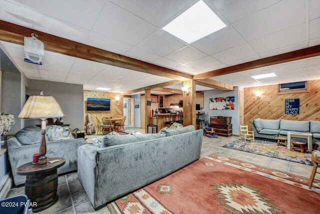 living room with a paneled ceiling, beam ceiling, light tile patterned floors, and wood walls