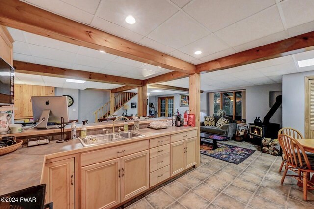 kitchen with sink, a paneled ceiling, a wood stove, beam ceiling, and light brown cabinets