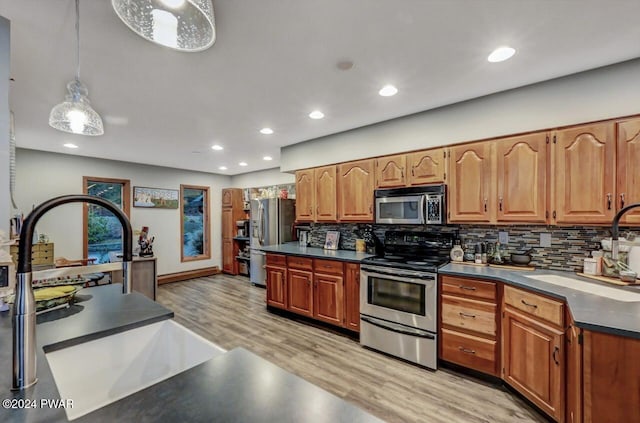 kitchen with appliances with stainless steel finishes, tasteful backsplash, sink, hanging light fixtures, and light wood-type flooring