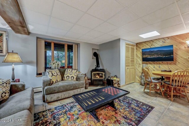 tiled living room featuring a baseboard heating unit, wooden walls, a paneled ceiling, and a wood stove