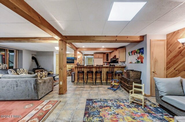 tiled living room featuring a wood stove, a drop ceiling, beam ceiling, and wood walls