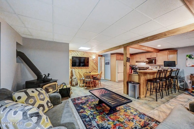 tiled living room with a wood stove, a paneled ceiling, and wooden walls