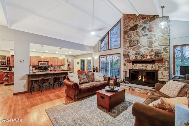 living room featuring a stone fireplace, sink, high vaulted ceiling, light hardwood / wood-style flooring, and beam ceiling