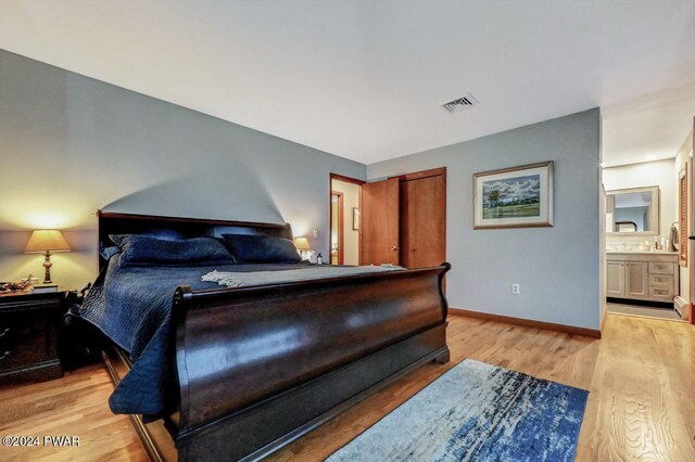 bedroom featuring connected bathroom and light hardwood / wood-style flooring