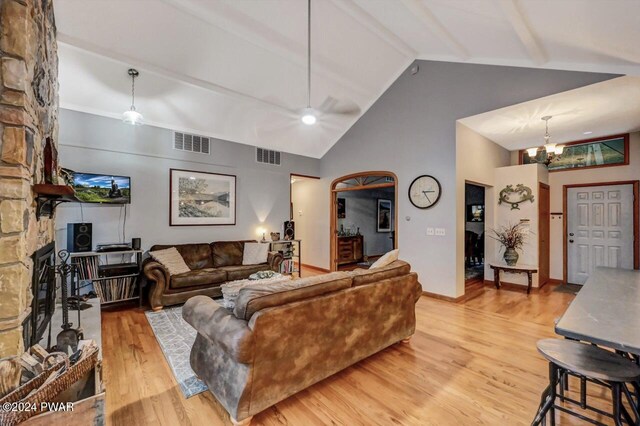 living room with ceiling fan with notable chandelier, high vaulted ceiling, a fireplace, beamed ceiling, and light wood-type flooring