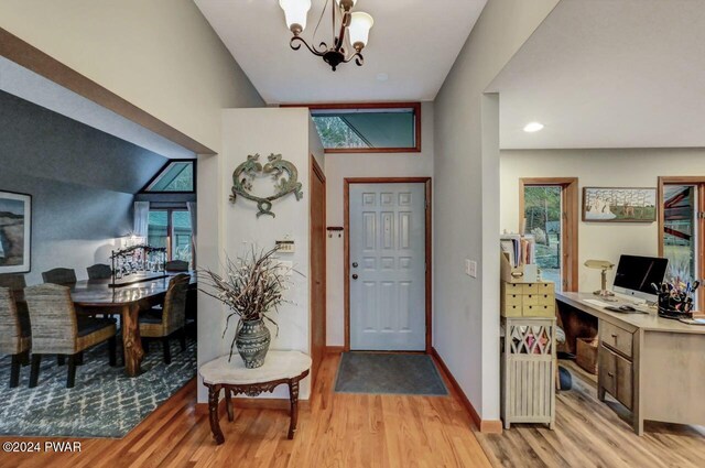 foyer with a notable chandelier, light hardwood / wood-style flooring, vaulted ceiling, and plenty of natural light