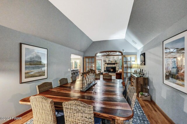 dining room featuring lofted ceiling, a stone fireplace, and dark hardwood / wood-style floors