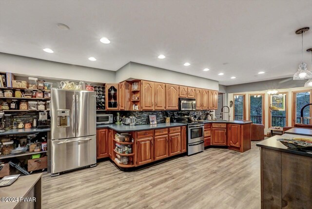 kitchen with appliances with stainless steel finishes, sink, backsplash, hanging light fixtures, and light hardwood / wood-style flooring