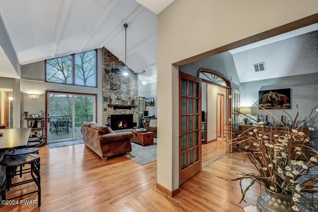 living room featuring high vaulted ceiling, a stone fireplace, light hardwood / wood-style floors, and beamed ceiling