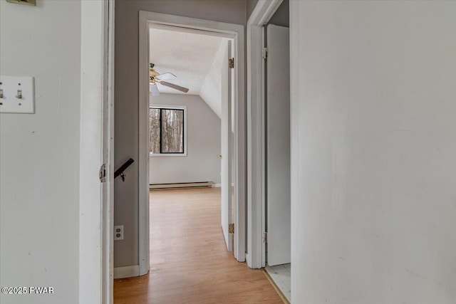 hallway with baseboard heating, vaulted ceiling, a textured ceiling, and light wood-type flooring