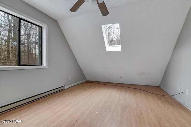 bonus room with ceiling fan, light wood-type flooring, vaulted ceiling with skylight, and baseboard heating