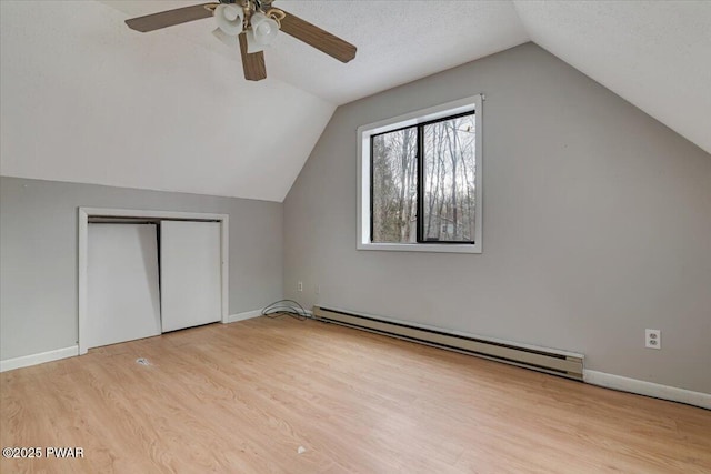 additional living space featuring a baseboard radiator, lofted ceiling, a textured ceiling, and light wood-type flooring