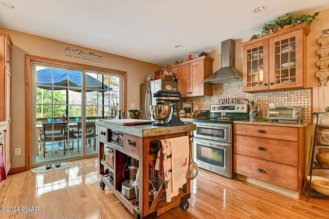 kitchen featuring wall chimney exhaust hood, light wood-type flooring, backsplash, and appliances with stainless steel finishes