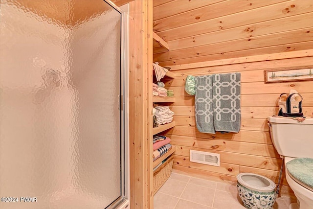 bathroom featuring tile patterned flooring, toilet, a shower with door, and wooden walls