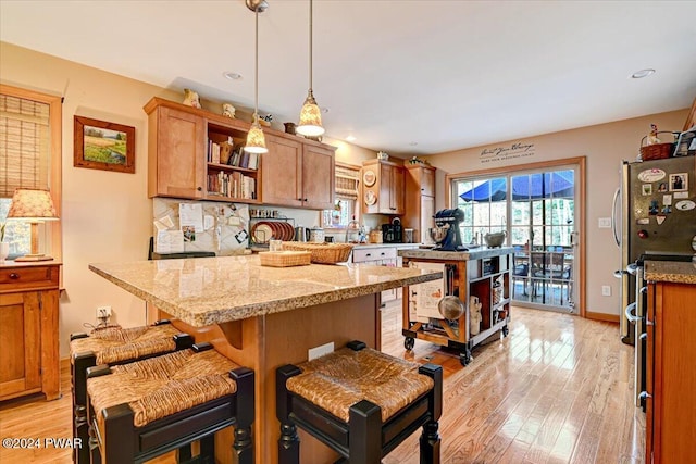 kitchen featuring pendant lighting, a kitchen breakfast bar, a kitchen island, light stone countertops, and light hardwood / wood-style floors